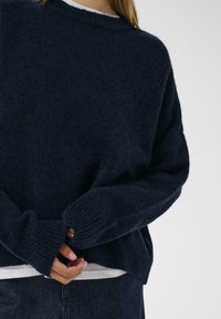 Tmavomodrý oversized sveter z mäkkej, štruktúrovanej tkaniny, s rebrovanými manžetami a lemom, okrúhlym výstrihom a voľným strihom.