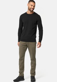 Suéter negro de manga larga con cuello redondo, combinado con chinos verde oliva y zapatillas negras. Textura suave, diseño ajustado.