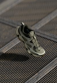 Olive green athletic shoe with mesh and rubber materials, lace-up design, cushioned sole, and a textured grip on the underside.