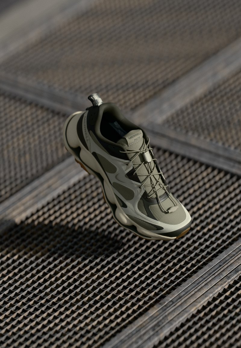 Olive green athletic shoe with mesh and rubber materials, lace-up design, cushioned sole, and a textured grip on the underside.