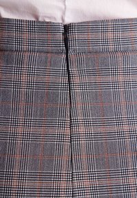 Czarna i biała tkanina w kratę z pomarańczowymi akcentami; posiada centralne zapięcie na zamek z tyłu i gładką fakturę.