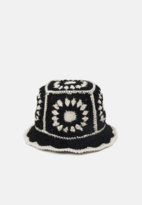 Chapeau seau au crochet fabriqué en fil noir et blanc, présentant un motif circulaire, un haut structuré et un bord festonné.