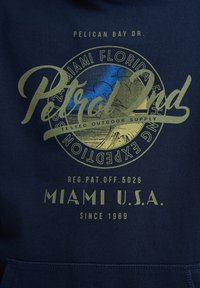 Sudadera de color azul marino con un gráfico que presenta "Pelican Bay Dr." y "Petrol" en verde, incluyendo un diseño de atardecer y texto sobre Miami, EE. UU.