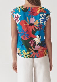 Blusa a maniche corte in un tessuto blu brillante con un motivo floreale che presenta fiori rossi, gialli, bianchi e pink, con una vestibilità rilassata.