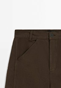 Pantaloni marroni con una texture liscia, chiusura con bottone e tasche angolate sul davanti. La vita è piatta con passanti per la cintura.