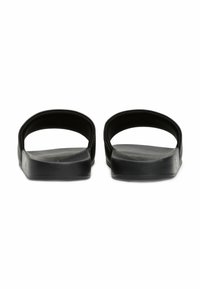 Sandali neri con suola piatta, design con punta aperta e due cinture curve. Realizzati in un materiale liscio e resistente con una finitura testurizzata.