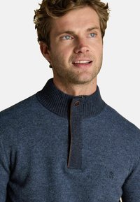 Tumši zila adīta džemperis ar augstu ribotu apkakli, pus-izjaukšanas aizdari un ādas akcentētu priekšpusi. Strukturēta auduma ar smalku rakstu.