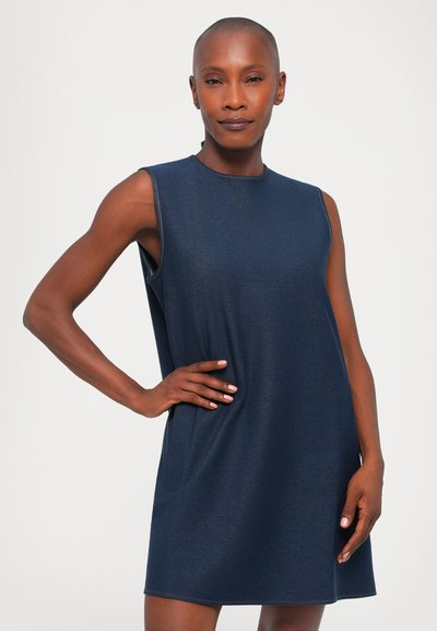 Muguru bez piedurknēm, tumši zila krāsā, izgatavots no mīksta auduma. Tam ir apaļa izgriezuma, sānu kabatas un brīvs piegriezums, līdz ceļgaliem. Gluda tekstūra.