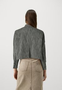 Jaqueta cinza cropped com uma superfície texturizada e colarinho, apresentando punhos com botões, combinada com uma saia de ganga bege com bolsos traseiros.