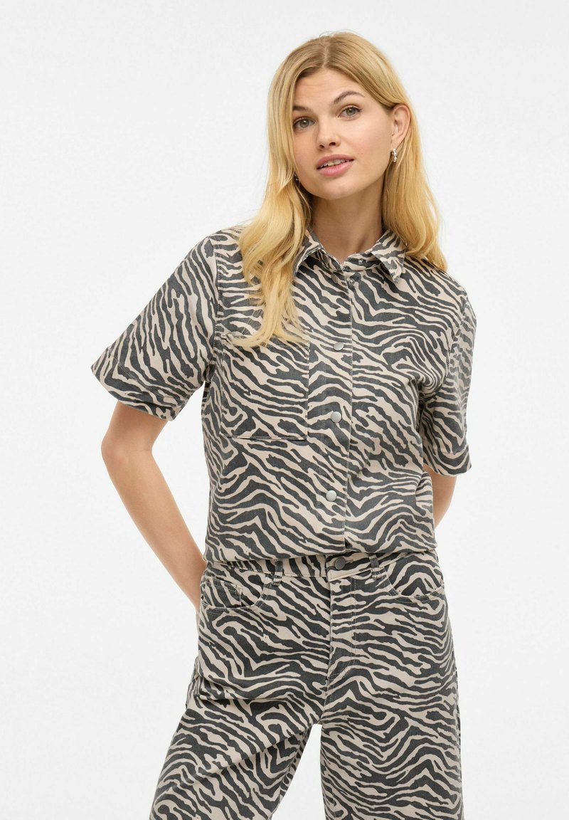 Kortsleevet skjorte og matchende bukser i zebra-print; stoffet ser mykt ut med en lys beige og mørkegrå fargekombinasjon. Knappelukking foran.