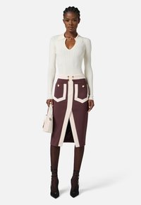 Top bianco a maniche lunghe aderente con colletto, abbinato a una gonna a tubino bordeaux con polsini crema e dettagli in metallo dorato.