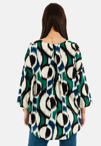 Blusa estampada de corte suelto, con audaces diseños circulares en negro, blanco, verde y azul sobre un fondo crema. Mangas de tres cuartos.