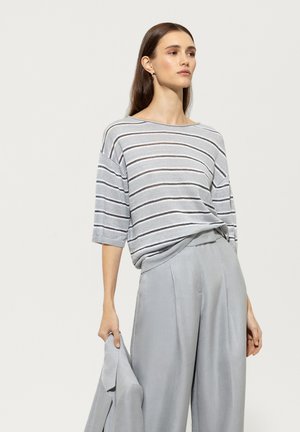 Grau- und weiß gestreiftes Strickoberteil mit weiten Ärmeln, kombiniert mit hellgrauen, hochtaillierten Hosen. Sanfte Textur, lockere Passform.