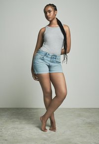 Shorts en denim bleu clair à taille haute et à cinq poches classiques, associés à un débardeur gris ajusté. Look décontracté et lisse.