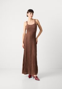Braunes, geripptes Maxikleid mit breiten Trägern, tailliertem Oberteil und ausgestelltem Rock. Kombiniert mit glänzenden roten High Heels. Glatte Textur.