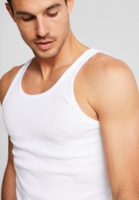 White ribbed tank top, cotton material, sleeveless design, fitted shape, smooth texture, and rounded neckline. No notable patterns or accents.
