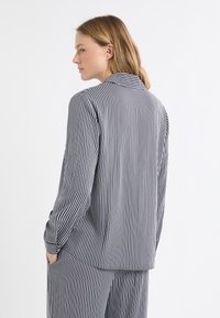 Bluzka w paski w kolorze granatowym i białym, z kołnierzykiem, długimi rękawami i luźnym krojem. Paski są pionowe, równomiernie rozmieszczone i teksturowane.