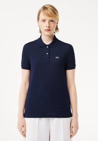 Granatowa koszulka polo wykonana z teksturowanej tkaniny, z klasycznym kołnierzykiem, trzema guzikami i małym zielonym logo na lewej piersi.