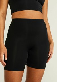 Svarta träningsoveralla i ett mjukt, elastiskt material. Har en midjehöjd som är mitt emellan och en åtsittande design som slutar strax ovanför knäet.