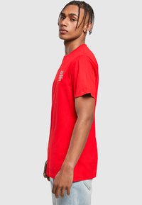 Camiseta de algodón roja con cuello redondo. Presenta mangas cortas y un logo en el frente. Textura suave y corte relajado.