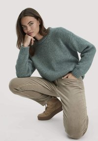 Gebreide trui in zacht teal, ronde halslijn, geribde manchetten; gecombineerd met tan corduroy broek en bruine enkellaarzen met stevige zolen.