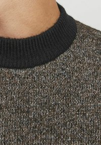 Suéter de punto con un oscuro cuello acanalado, tejido texturizado en marrón y crema con un patrón de colores mixtos, primer plano del área del cuello.