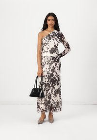 Robe asymétrique en crème avec des motifs abstraits noirs. Associée à un sac à main noir et des escarpins beiges à bout pointu. Tissu lisse et léger.