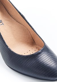 Zapato de tacón de cuero azul marino con superficie texturizada, punta afilada y un interior suave que presenta pequeñas perforaciones para la transpirabilidad.