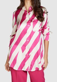 Chemise rayée rose et blanche avec un col, fermeture �à boutons sur le devant et une poche poitrine. Fabriquée en tissu lisse ; les manches sont retroussées.