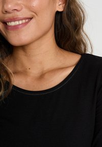 T-shirt noir avec un col rond et des détails de couture légère contrastante. Gros plan sur le col et la zone de l'épaule.