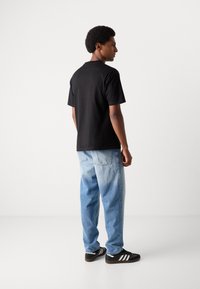 Black short-sleeve T-shirt with a crew neckline, worn with light blue faded denim jeans and black sneakers featuring white stripes.