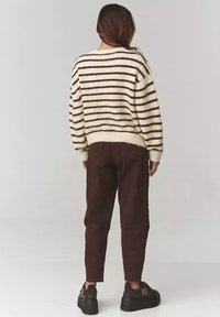 Beżowy sweter z dzianiny w brązowe paski, luźny krój, okrągły dekolt i ściągacze. Noszony z ciemnobrązowymi spodniami i czarnymi butami na platformie.