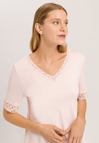 Camiseta rosa para mujer con escote en V adornado con un ribete de encaje y detalles de encaje en las mangas cortas. Textura de tejido suave y suave.