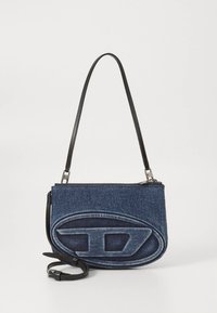 Denim handbag with a textured blue exterior, featuring a prominent oval design and a detachable black leather strap. Zipper closure on top.