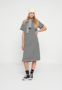 Φόρεμα μπλούζας με ασπρόμαυρες ρίγες, μήκος μέχρι το γόνατο, με κοντά μανίκια. Αξεσουάρ: ανοιχτό κίτρινο σκούφο, γκρίζο κασκόλ και μαύρα sneaker με ψηλή σόλα.