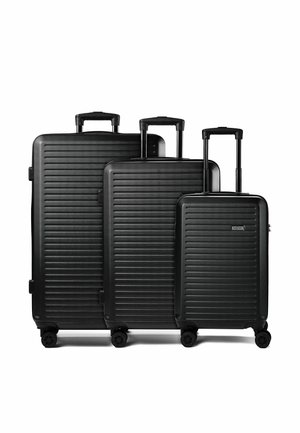 Tre valigie rigide nere di dimensioni diverse con scanalature orizzontali, manici telescopici estesi e quattro ruote girevoli ciascuna.