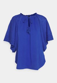 Blusa blu royal con maniche corte ricamate, scollatura arricciata, apertura a forma di chiave e dettagli con frange. Realizzata in tessuto leggero.