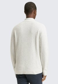 Pull en maille texturée gris clair avec col et poignets côtelés. Présente un motif légèrement moucheté. Coupe ajustée avec fentes sur les côtés.