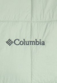 Šviesiai žalia, siuvinėta medžiaga su subtilia tekstūra. Yra išsiuvinėtas "Columbia" logotipas tamsiai pilka siūlais. Matomos siūlės.