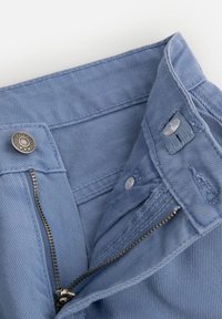 Jasnoniebieskie dżinsy z zamkiem błyskawicznym, metalowym zapięciem i kontrastową, teksturowaną podszewką. Posiadają detale w postaci przeszyć.