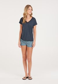 T-shirt blu navy con scollo a V e maniche arrotolate, abbinato a pantaloni corti blu a fantasia con disegni geometrici. Il modello indossa infradito nere.