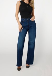 Svart ärmlös topp kombinerad med högmidjade mörkblå denimjeans. Jeans har en rak passform och en subtilt urtvättad textur.