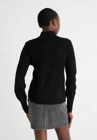 Pulover negru din tricot cu guler înalt, textură cu nervuri și mâneci lungi, asortat cu o fustă din denim gri cu accente cu ținte.