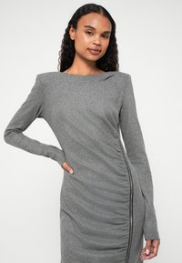 Vestido cinza de manga longa com decote barco, franzidos laterais e detalhe de zíper exposto ao longo do lado esquerdo. Tecido suave e texturizado.