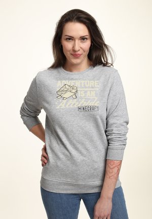 Szara bluza z napisem "PRZYGODA TO POSTAWA" oraz grafiką z gry Minecraft. Dopinane ściągacze na mankietach i dole. Luźny krój.