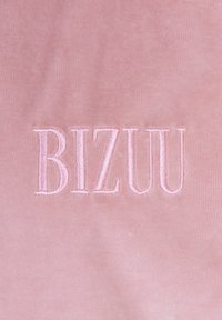 Roze stof met een zacht gestructureerd oppervlak en een geborduurd "BIZUU" logo in bijpassend roze, die een minimalistisch ontwerp toont.