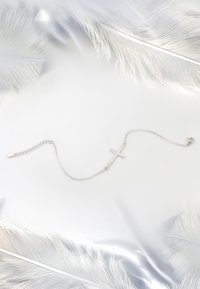 Bracciale in argento con una delicata catena, caratterizzato da un design semplice. La croce è centrata sulla catena, posata su morbide piume bianche.