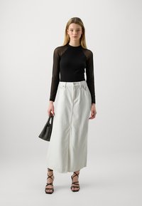 Haut en maille noir à manches longues associé à une jupe maxi en denim blanche, sandales noires à lanières et un sac à main noir texturé.