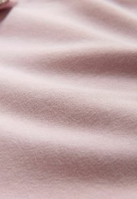 Zacht, lichtroze gebreide stof met een subtiele textuur en zachte plooien die vloeiende schaduwen creëren.