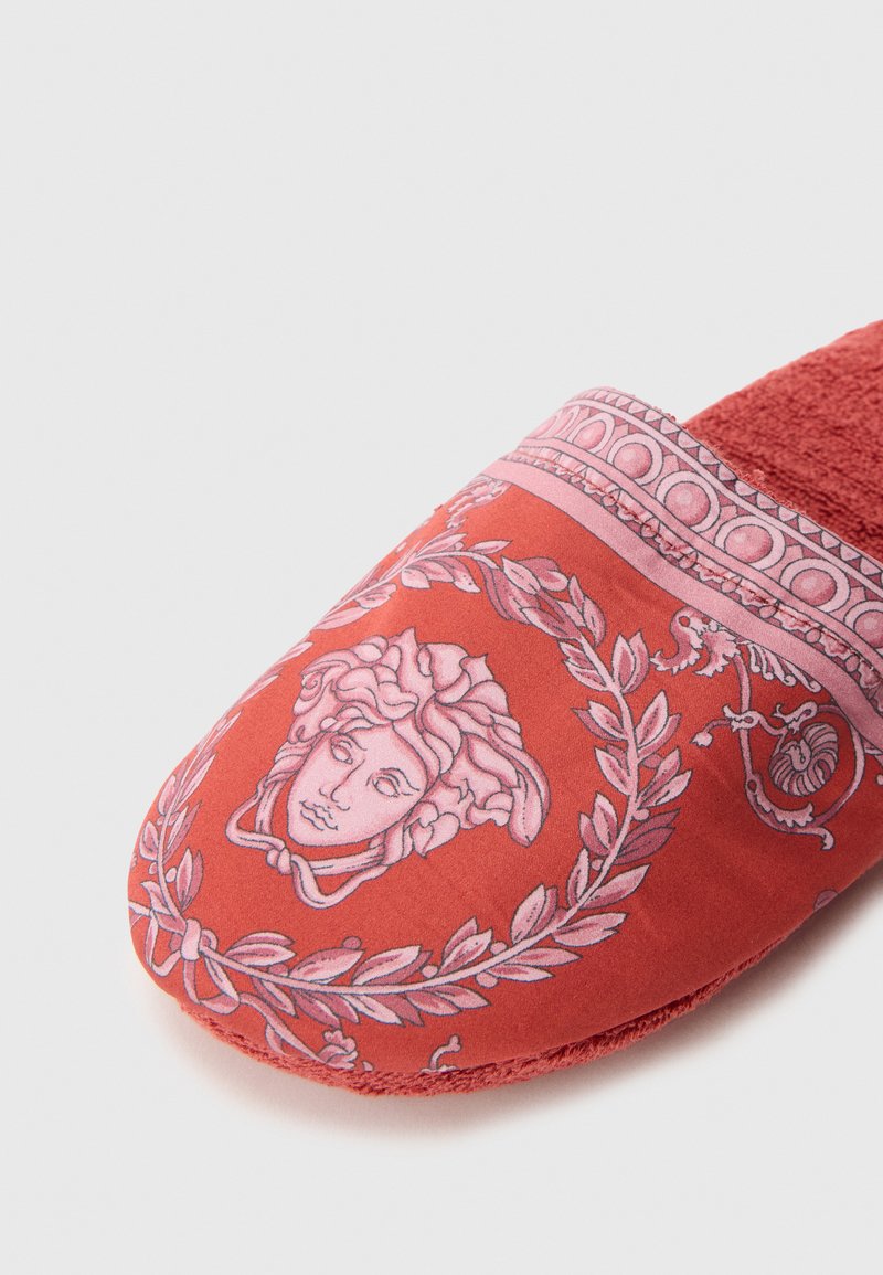 Red fabric slipper featuring a pink classical face graphic surrounded by laurel leaves, with a textured interior and smooth upper.